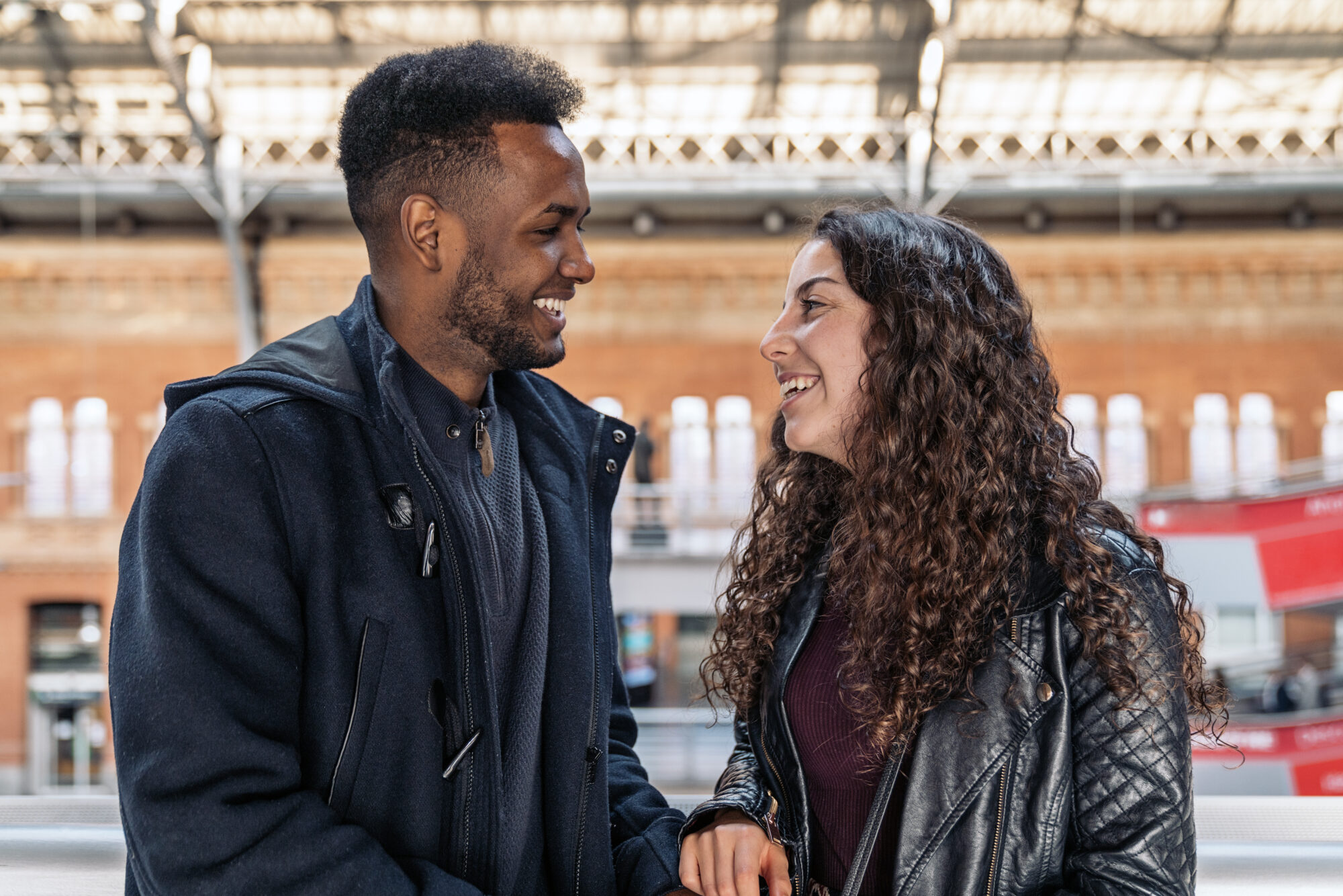 Man and woman smiling and engaging in a friendly conversation outdoors, highlighting a natural connection in a casual urban setting.