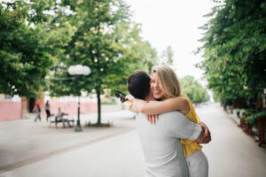 An American couple embracing affectionately outdoors, with the woman smiling brightly, showing a loving and happy moment between them.