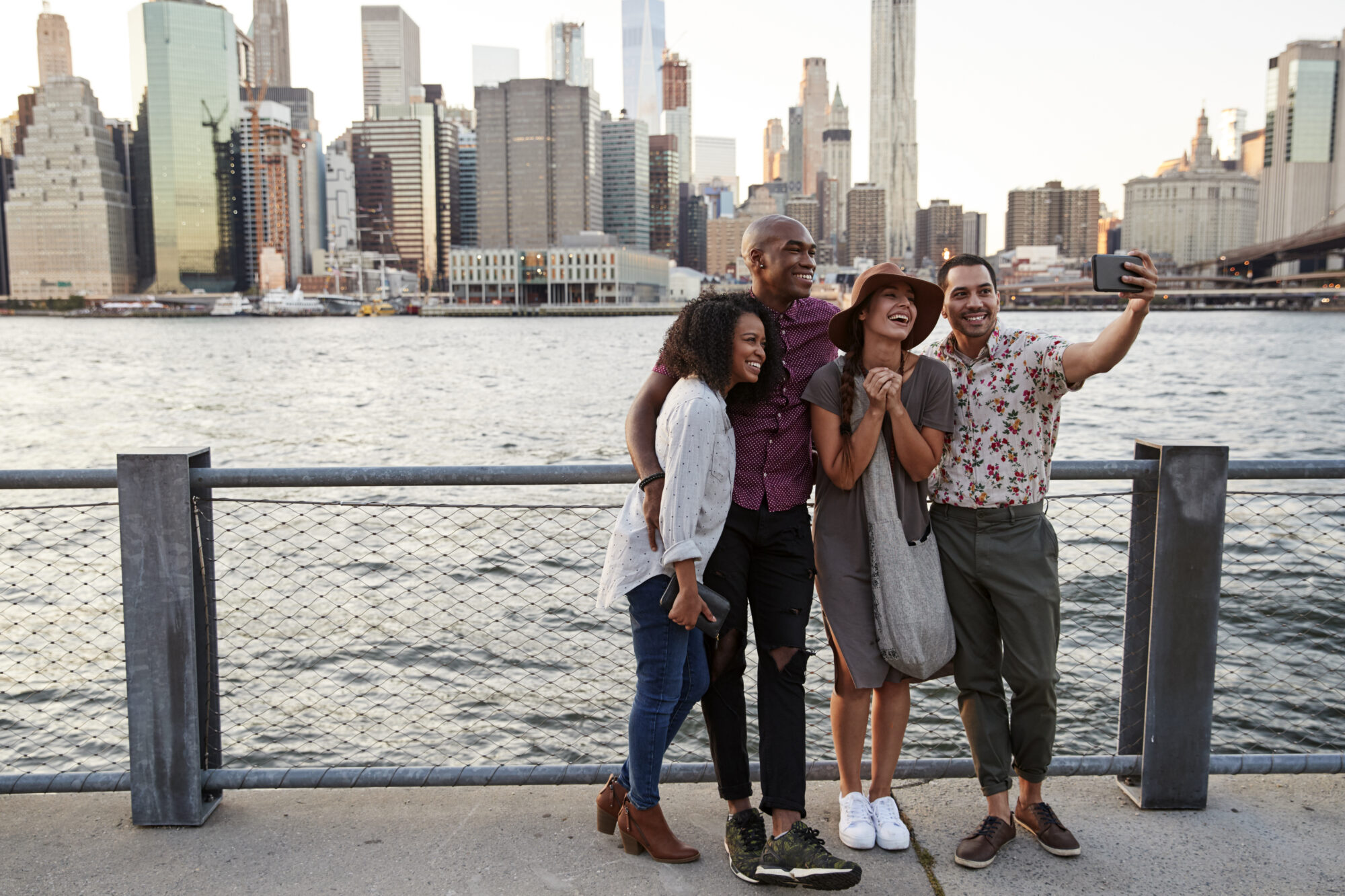 A group of friends posing for a selfie in front of the Manhattan skyline, located in New York City, USA, representing friendship, diversity, and shared experiences in an iconic urban setting.