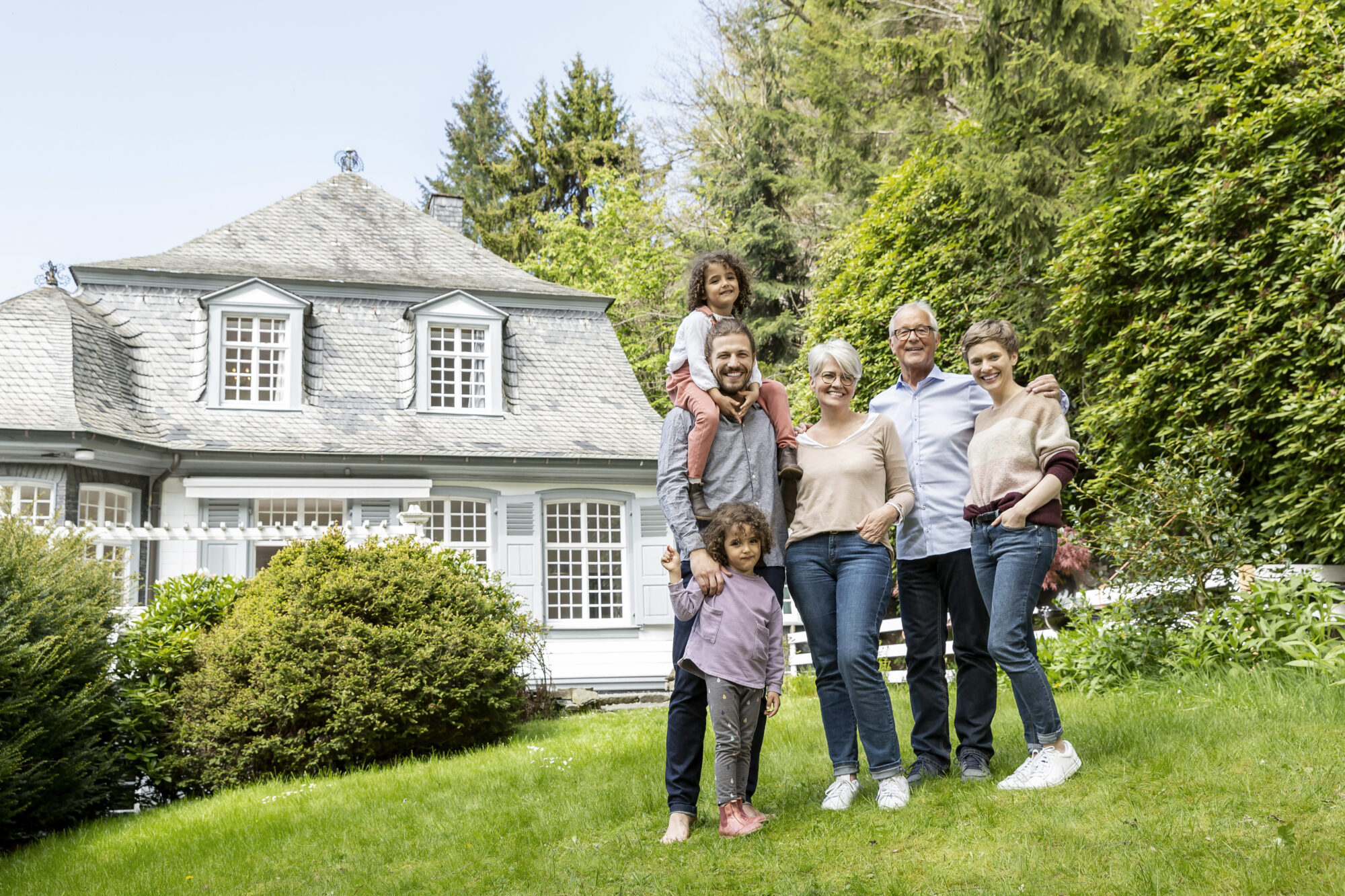 A happy extended family standing in the garden of their home, symbolizing unity, prosperity, and the fulfillment of the American Dream